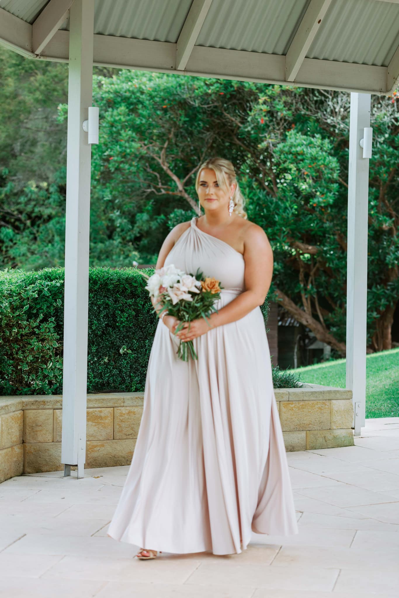Woman in a flowing champagne bridesmaid gown holding bouquet, stylish convertible dress Australia