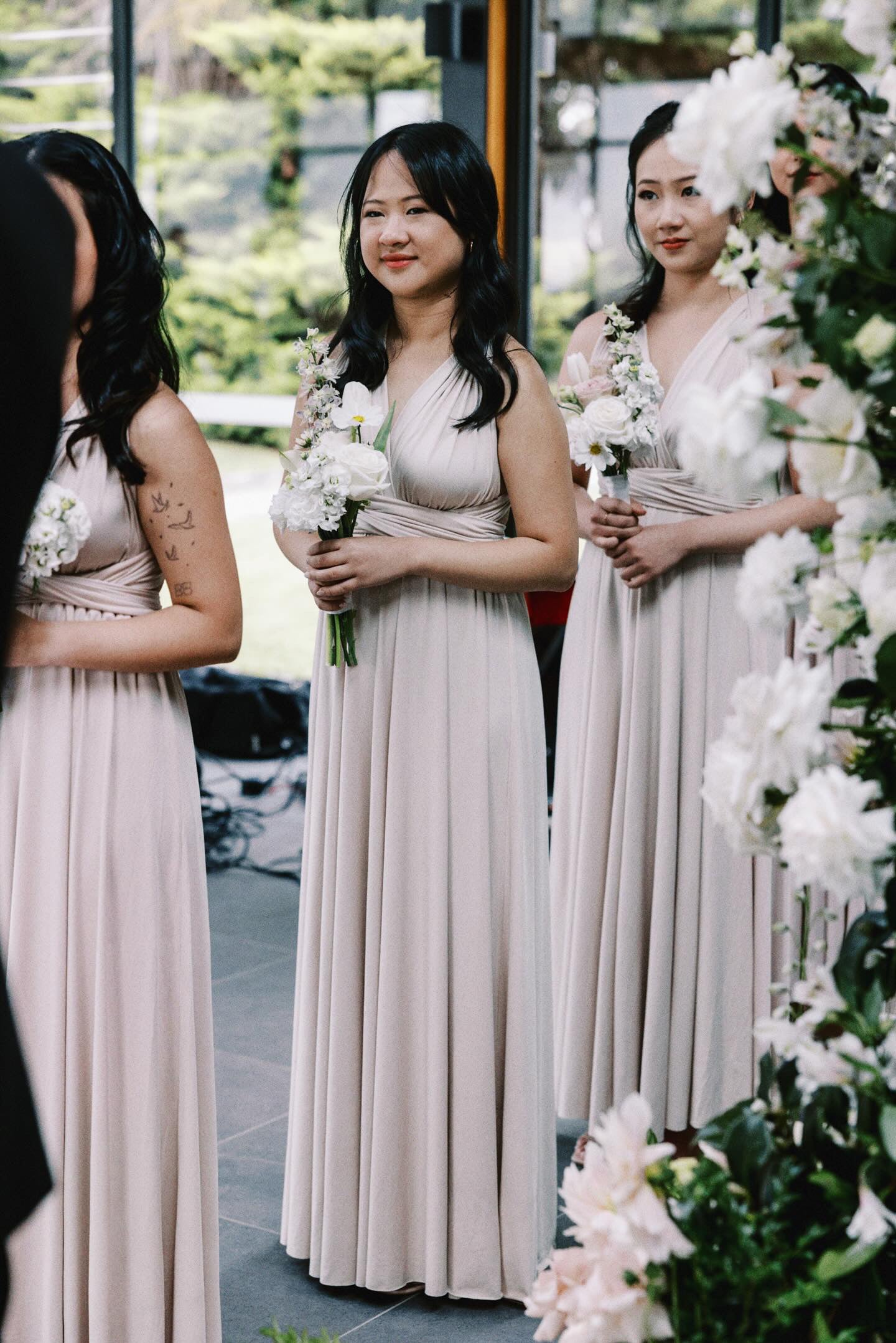 Three bridesmaids in champagne bridesmaid gown holding bouquets, showcasing convertible dress Australia