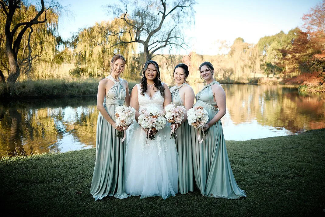 Four women in formal dresses holding bouquets wearing Eucalyptus Infinity Gown, a convertible green bridesmaid dress