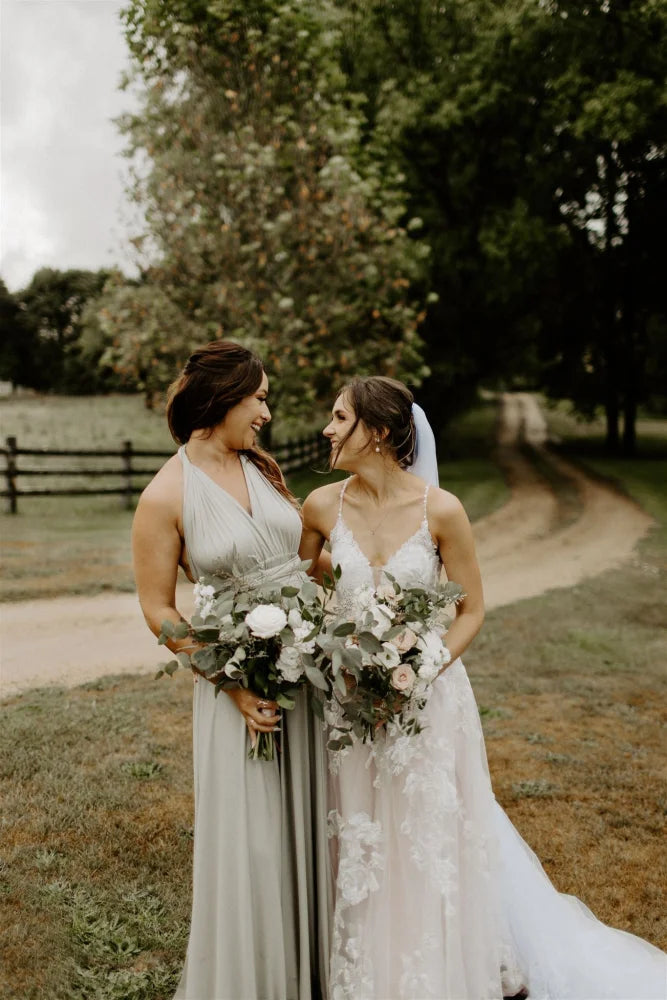 Two women in wedding attire holding bouquets wearing the Eucalyptus Infinity Gown, a convertible green bridesmaid dress