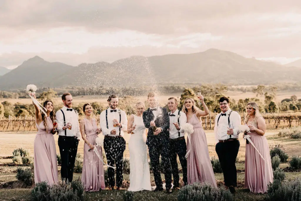 Wedding party celebrating with champagne in a vineyard wearing blush pink infinity bridesmaid dress
