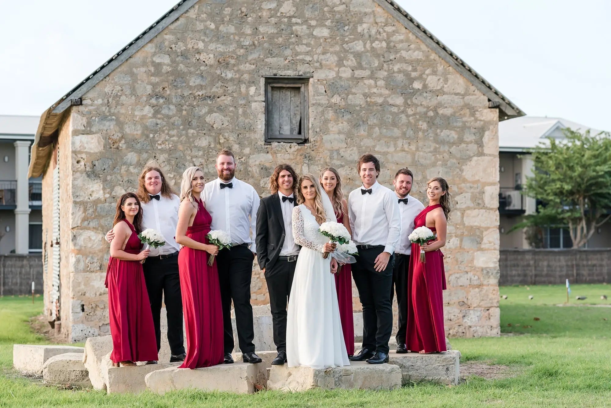 Wedding celebration featuring bride, groom, and guests in front of stone building with infinity dress Australia