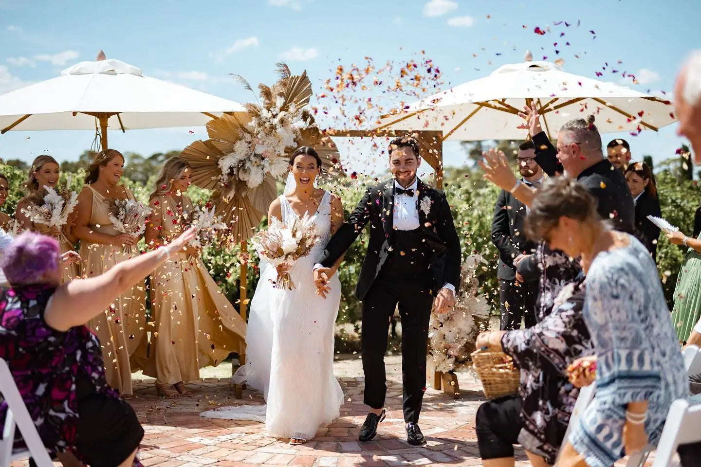 Happy bride and groom walking down aisle with confetti, showcasing infinity dress Australia