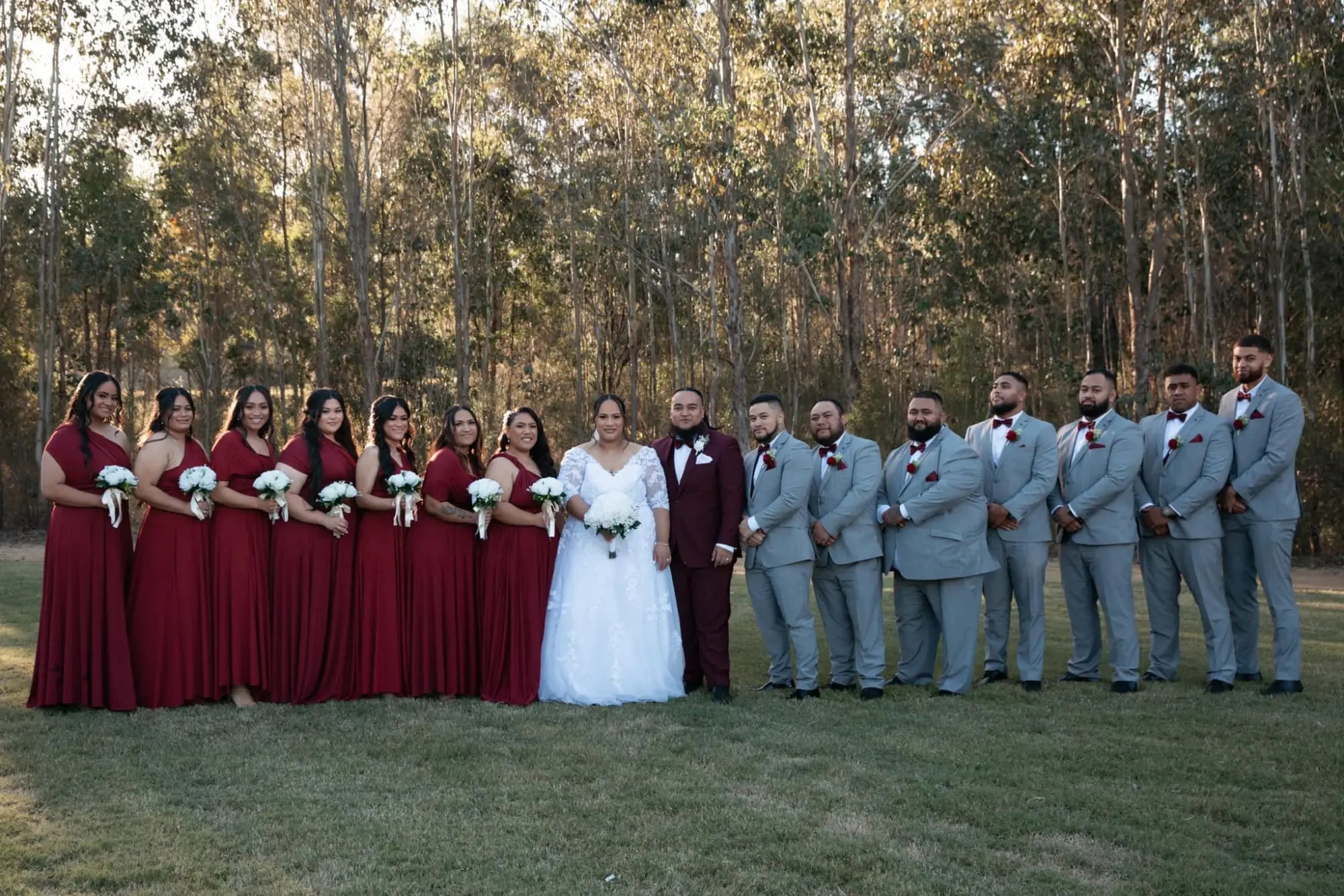 Wedding party outdoors in luxe satin burgundy infinity gown with bridesmaids and groomsmen