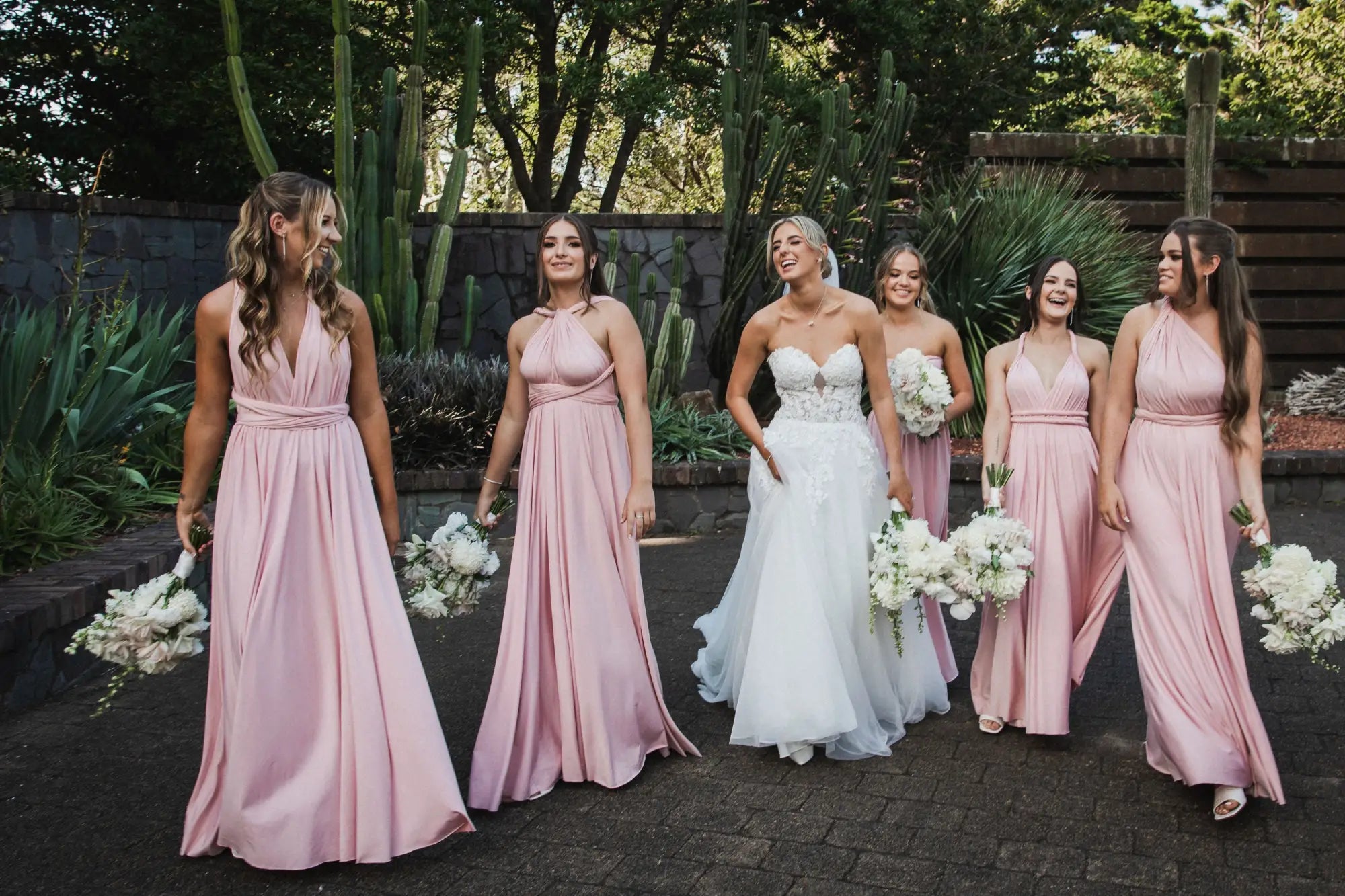 Six women in pink infinity dresses and a white wedding gown holding bouquets at Matisse and Ryan