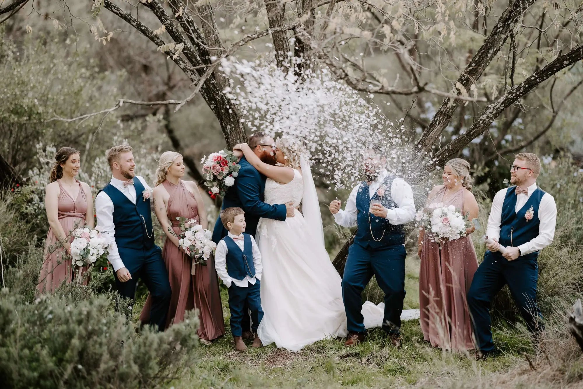 Joyous wedding party with couple sharing a kiss under confetti, featuring infinity dress Australia