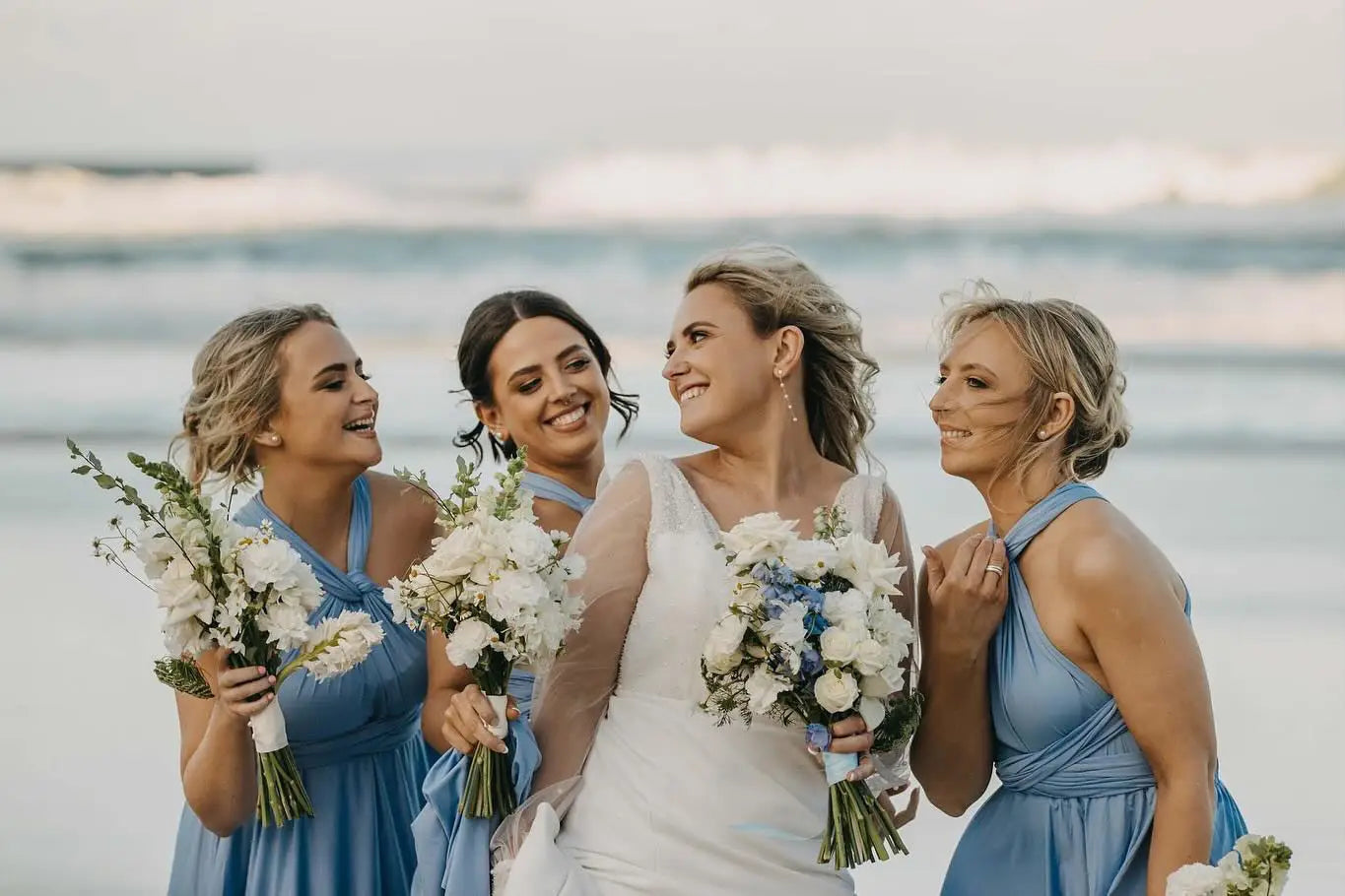 Four women in wedding attire holding bouquets, showcasing infinity bridesmaid dress in Australia