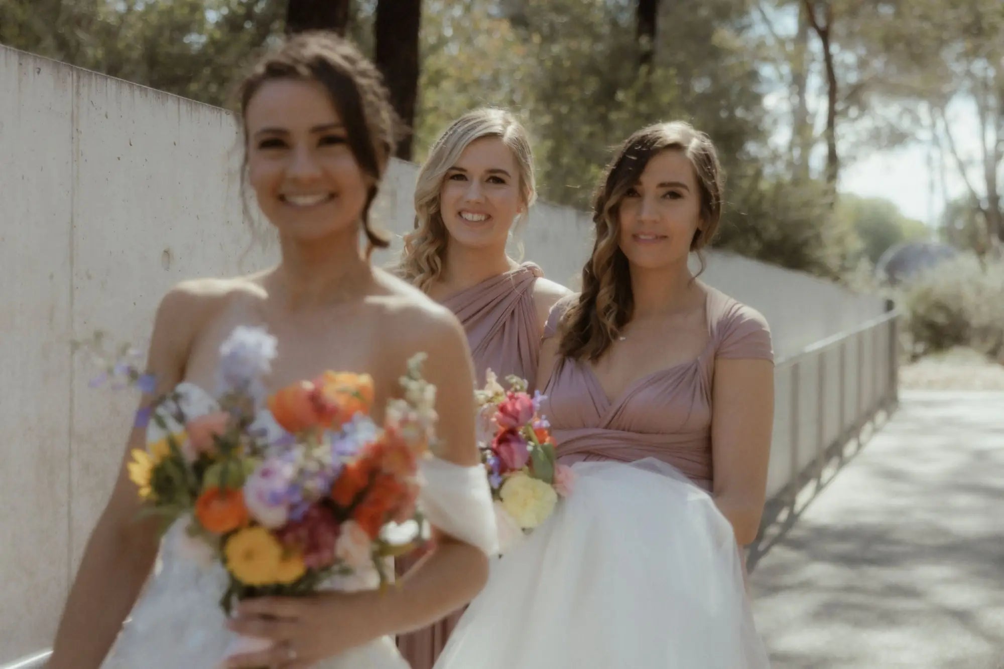 Three women in wedding attire holding bouquets wearing infinity dresses in Tara and Lachlan article