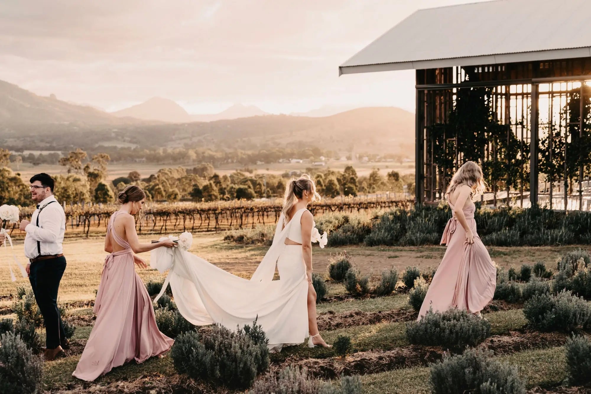 Group of people in formal attire walking through a field at sunset, showcasing infinity dress Australia