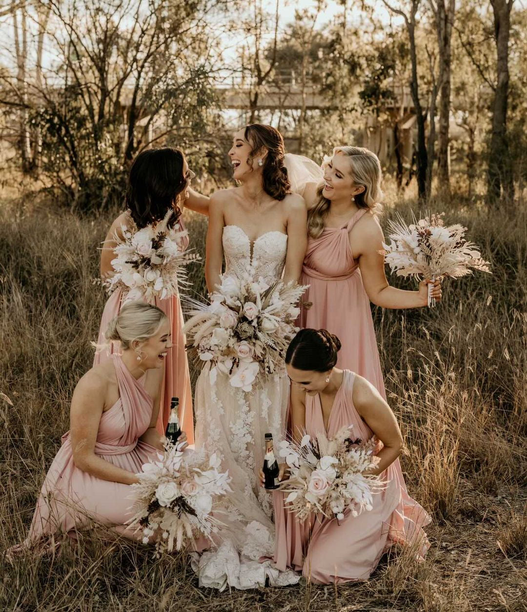 Bride in strapless white lace gown with four blush pink bridesmaid infinity gowns and dried flower bouquets