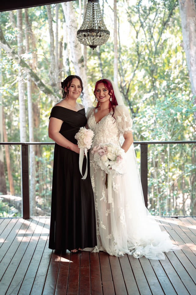 Two women in formal attire with bouquets, showcasing a Black Infinity Gown and multiway bridesmaid style