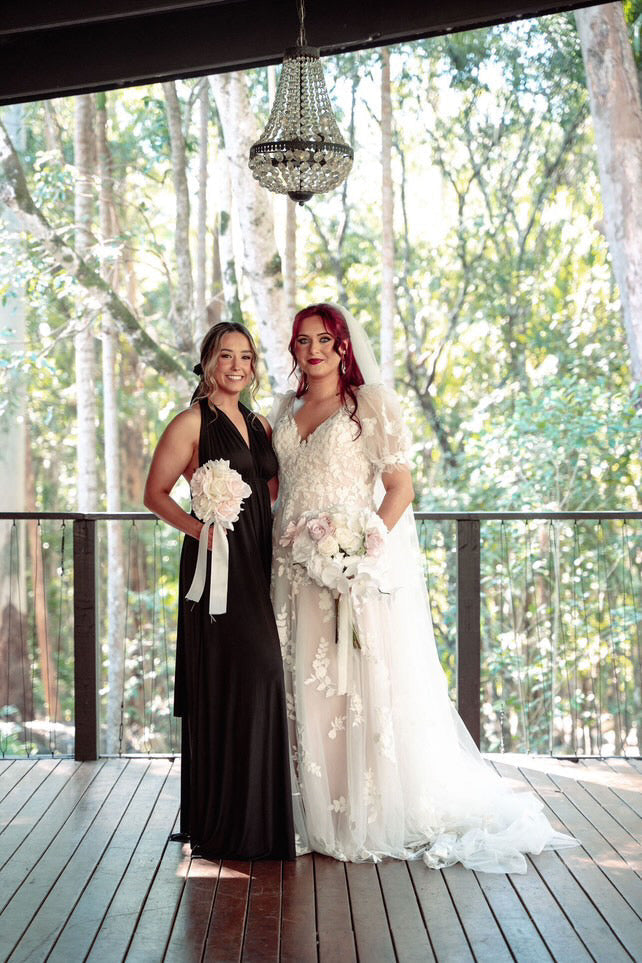 Two women in formal attire holding bouquets wearing Black Infinity Gown, perfect multiway bridesmaid convertible dress