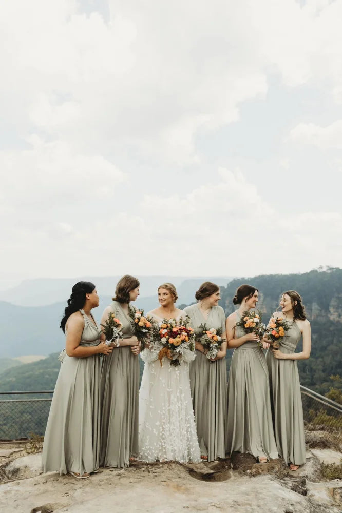 Bride in a white lace infinity gown with five bridesmaids in green convertible dresses