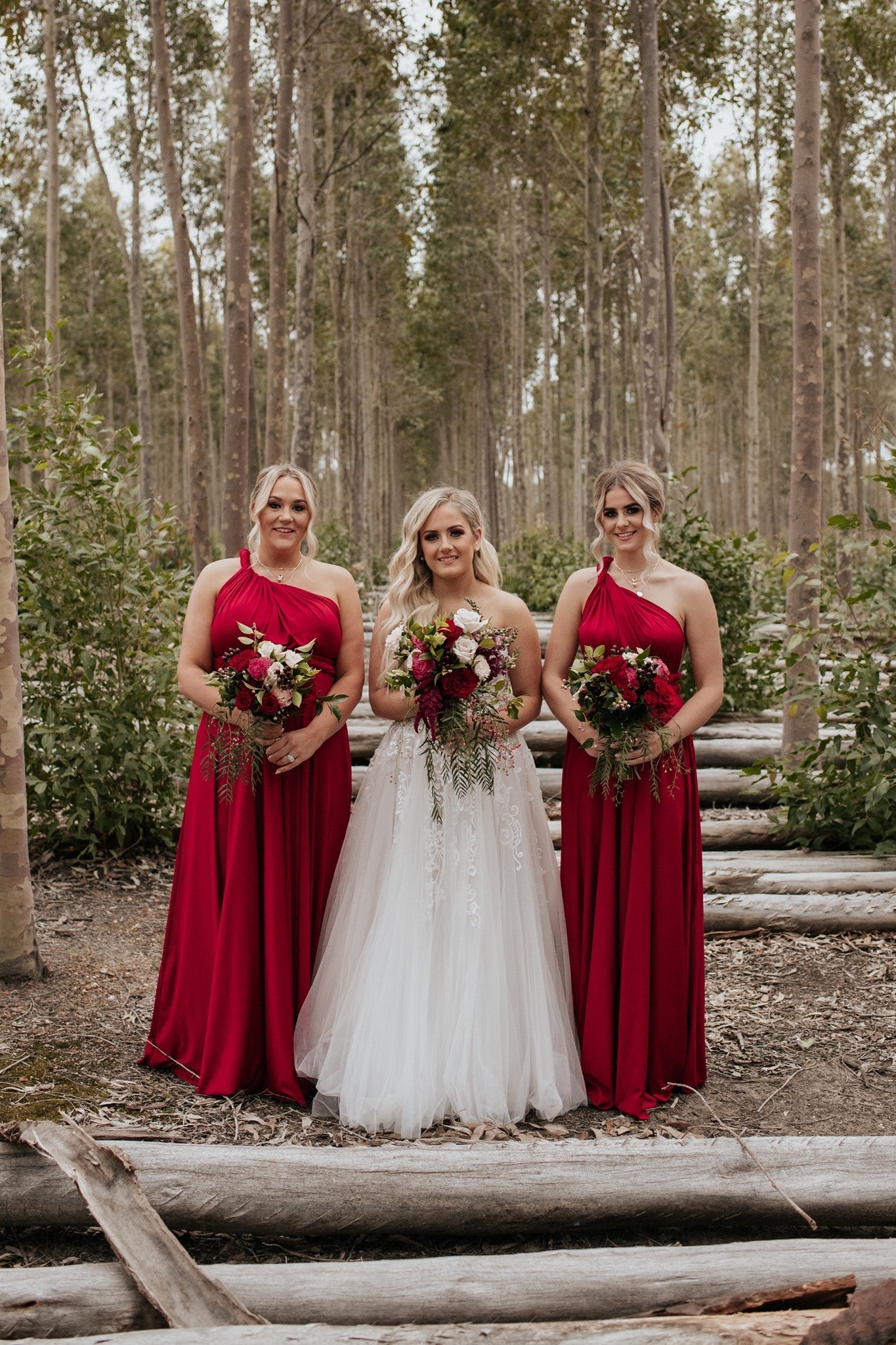 Three women in Wine Infinity Gown multiway bridesmaid convertible dresses holding bouquets
