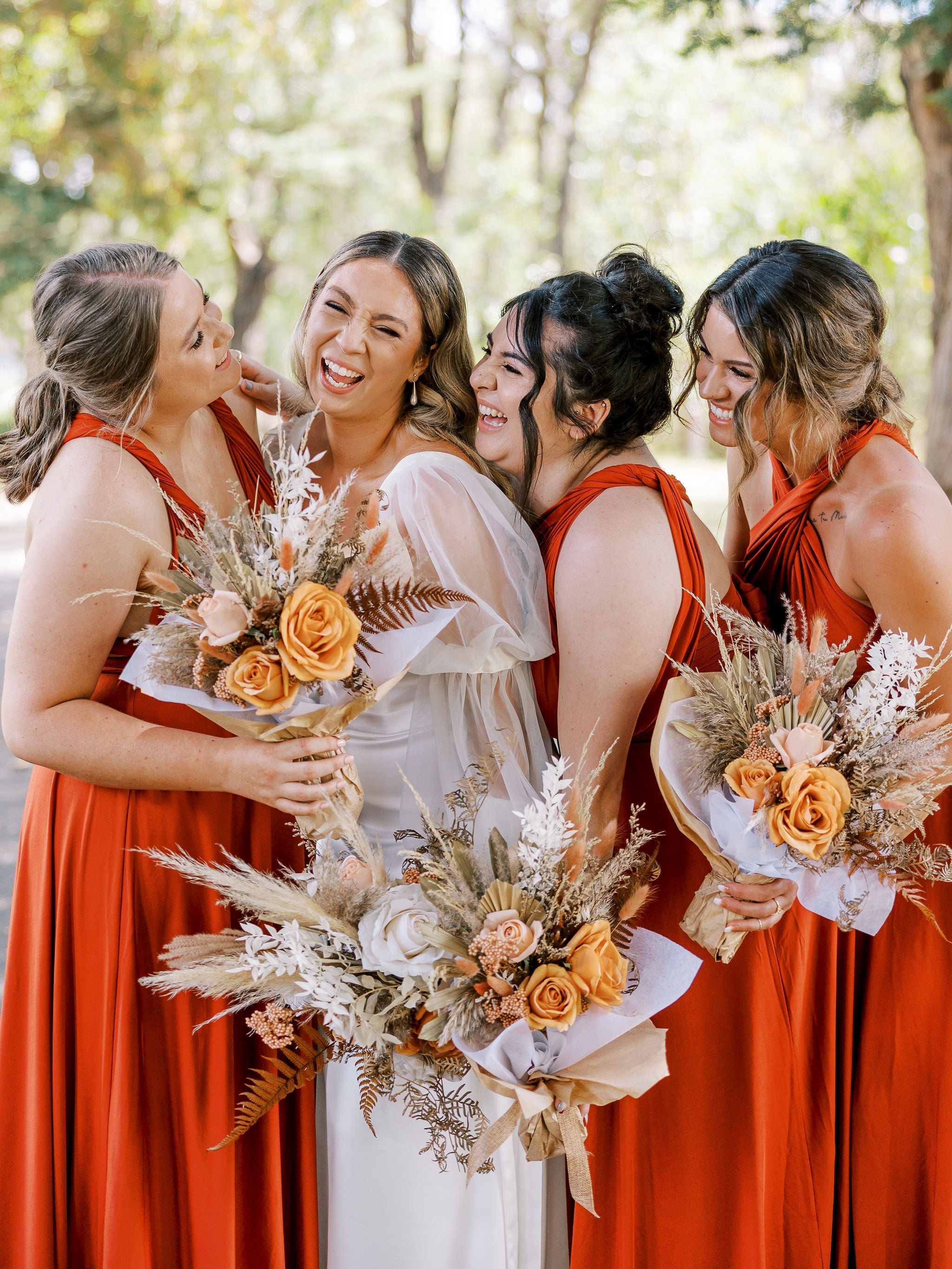 Five women in rust-colored multiway bridesmaid and infinity gowns laughing together
