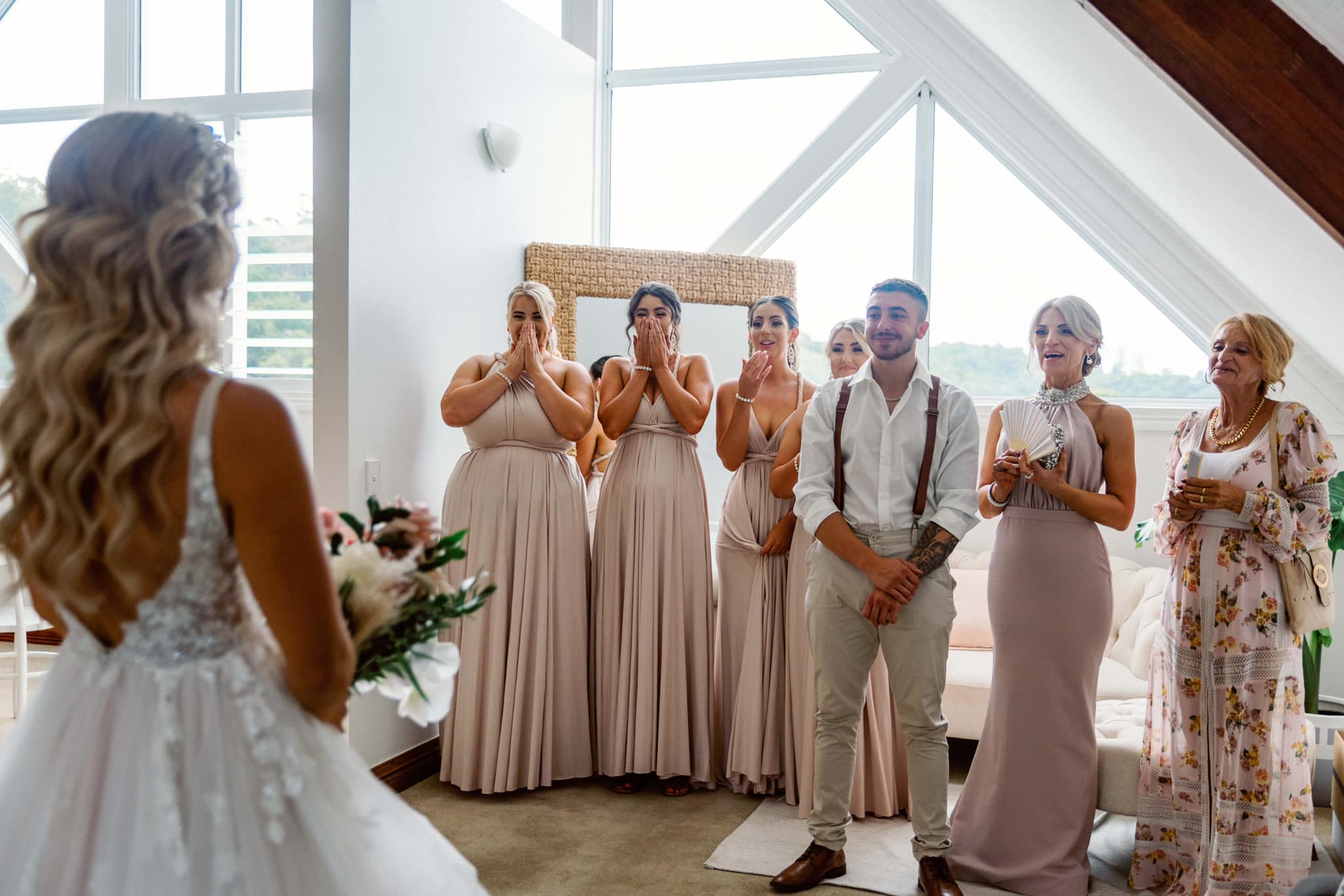 Bride in Champagne Infinity Gown with floral bouquet facing wedding guests, perfect multiway bridesmaid dress