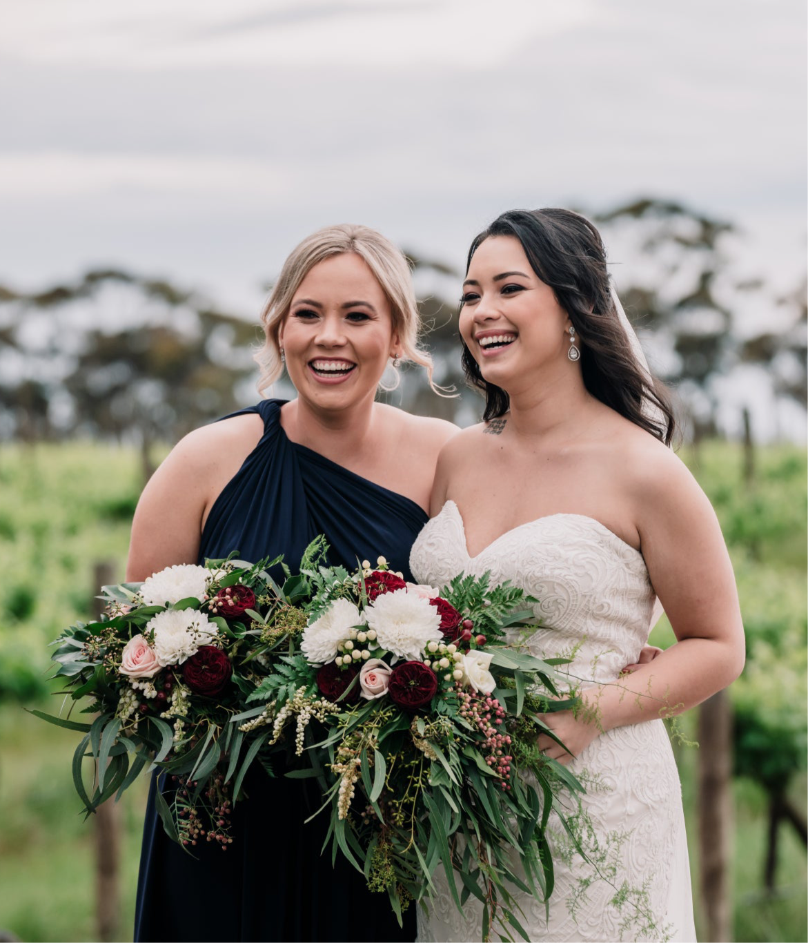 Two women in Navy Infinity Gown and wedding dress holding colorful bouquets