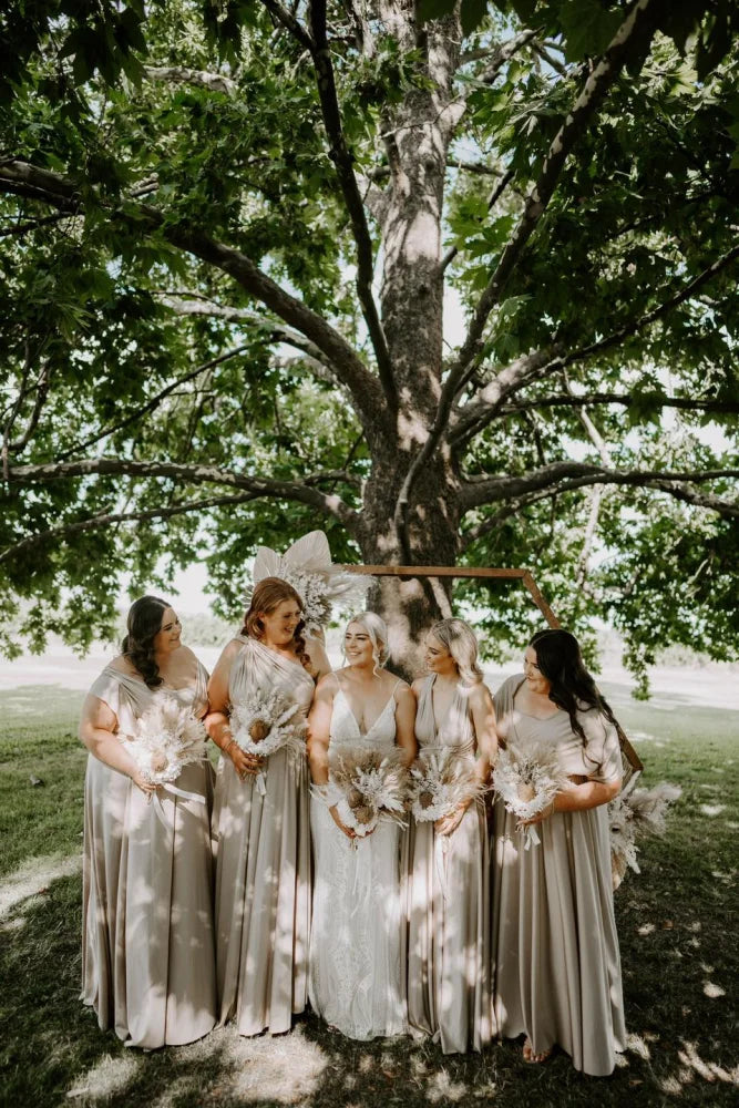 Five women in light-colored infinity gowns holding bouquets under a decorative arch, perfect for multiway bridesmaid dresses in Australia